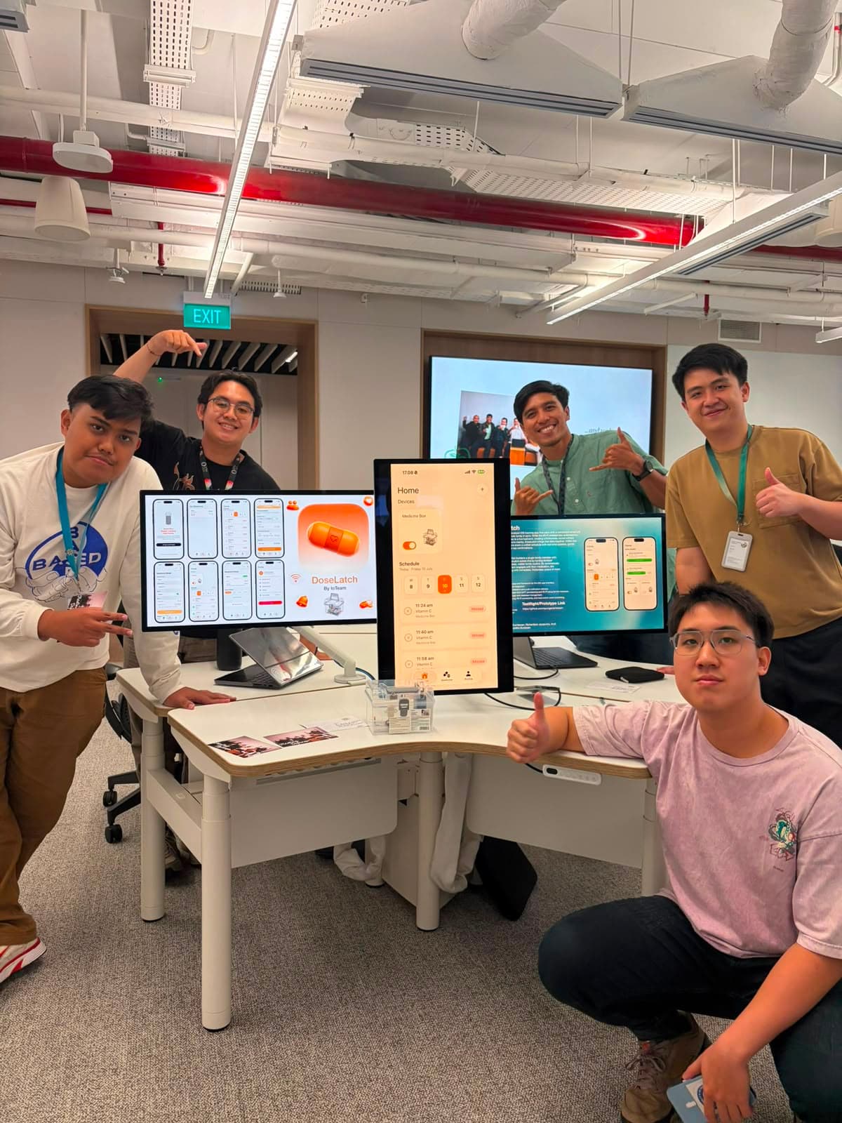 The DoseLatch demo stand: the app showcase on one screen, the live Home schedule on a portrait display, and the pill box on the desk